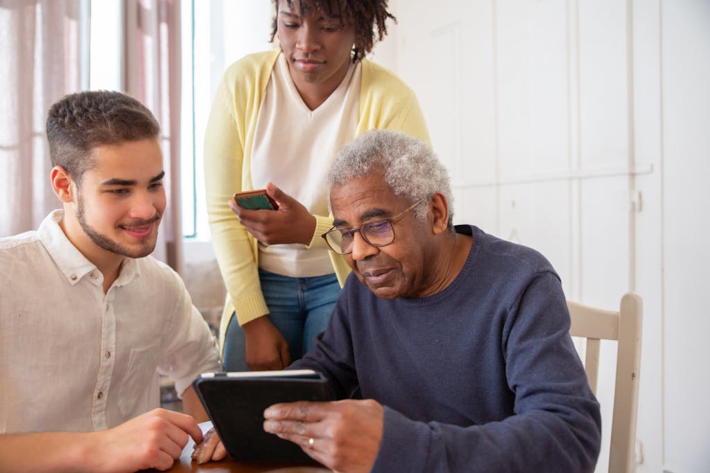 Senior receiving help with technology from a diverse group at home.